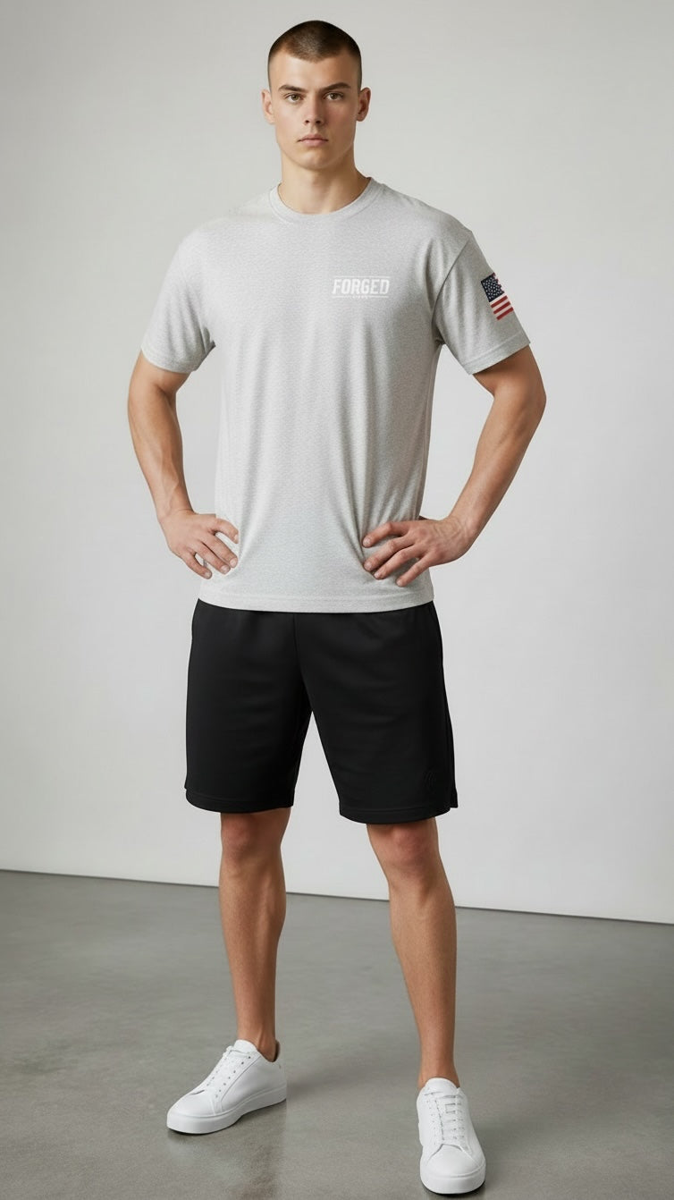 Model wearing a Forged By God grey crewneck t-shirt with a small chest logo and American flag patch on the sleeve.