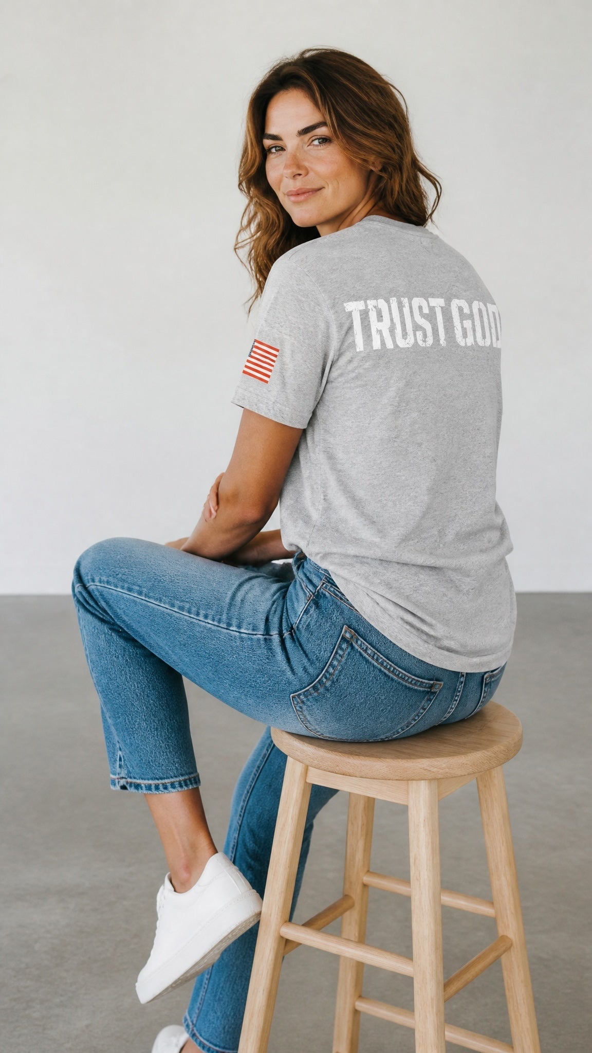 Forged By God grey crew neck t-shirt with Trust God back print and American flag sleeve detail on a seated woman