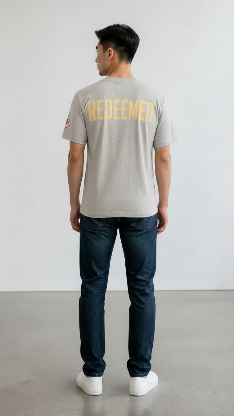 Model wearing Forged By God grey cotton t-shirt with yellow Redeemed graphic on back and American flag sleeve detail