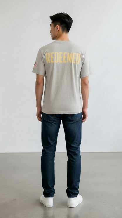 Model wearing Forged By God grey cotton t-shirt with yellow Redeemed graphic on back and American flag sleeve detail