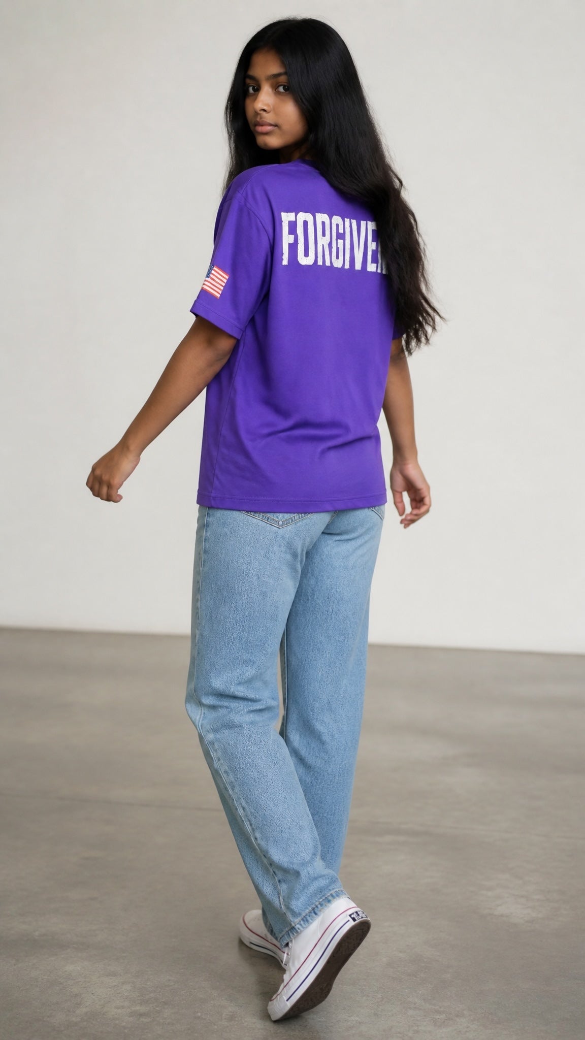 Forged By God purple crewneck t-shirt with Forgiven graphic on back and American flag sleeve patch on a young woman